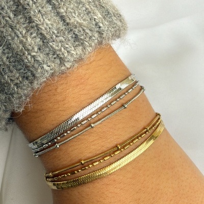 Conjunto de pulseiras finas prateadas e douradas no pulso de mulher com camisola cinza