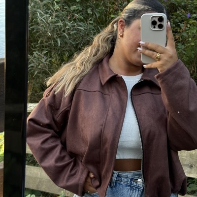 casaco castanho curto com top branco e calças de ganga, em ambiente exterior