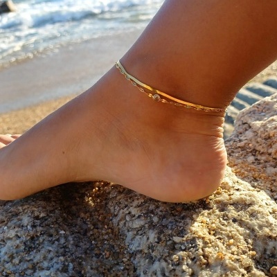Tornozeleira dourada num tornozelo sobre rochas na praia
