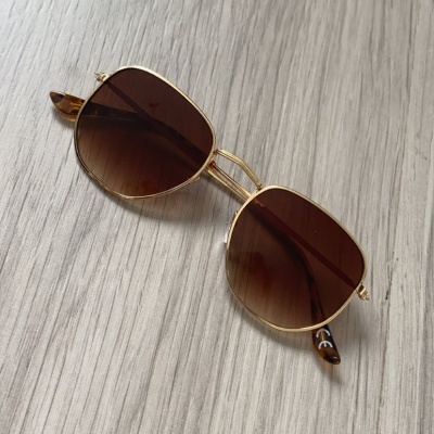 Óculos de sol com armação dourada e lentes castanho degradê sobre madeira clara
