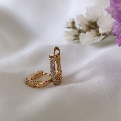 Brincos dourados com pedras transparentes sobre tecido branco e flores