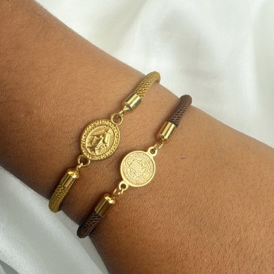 Duas pulseiras de cordão trançado com medalhões dourados em relevo no pulso.