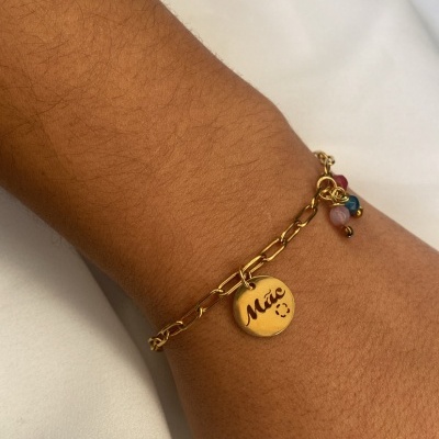 Pulseira dourada com pendente 'Mãe' em pulso sobre tecido branco