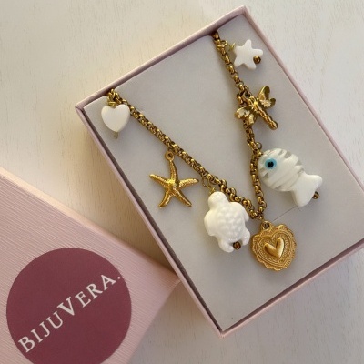 Colar dourado com vários pingentes brancos e dourados dentro de caixa rosa BIJUVERA