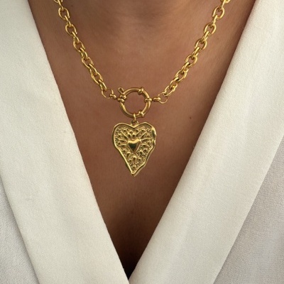 Colar dourado com pendente de coração texturizado sobre camisa branca