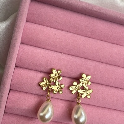 Brincos dourados com flores e gotas de pérola num suporte rosa