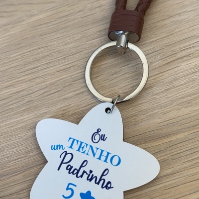 Chaveiro estrela branca com texto em azul e preto e cordão castanho trançado