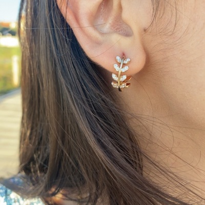 Brinco em metal dourado com folhas e pedras brilhantes numa orelha de mulher
