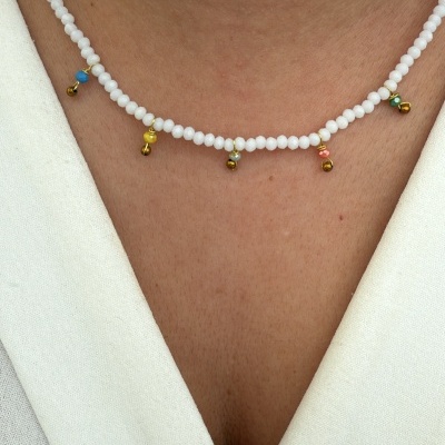 Colar de contas brancas com pendentes coloridos numa pessoa com camisa branca.