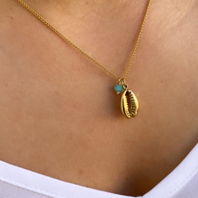 Colar com concha dourada e pedra azul sobre pele clara e roupa branca