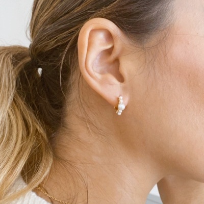 Brincos de pérolas pequenas em argola numa orelha feminina