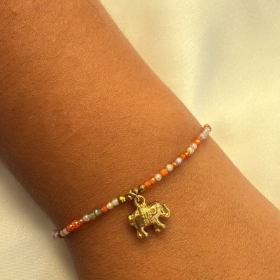 Pulseira de contas coloridas com pendente de elefante dourado no pulso.