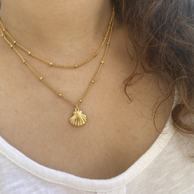 Colar duplo dourado com pendente de concha usado no pescoço