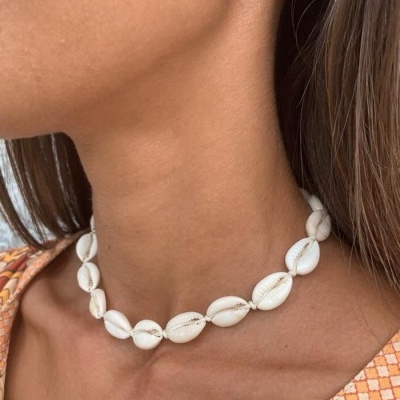 Gargantilha de conchas brancas naturais no pescoço de mulher com padrão laranja na roupa.