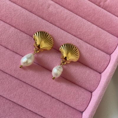 Brincos dourados em forma de concha com pérolas penduradas em suporte rosa aveludado