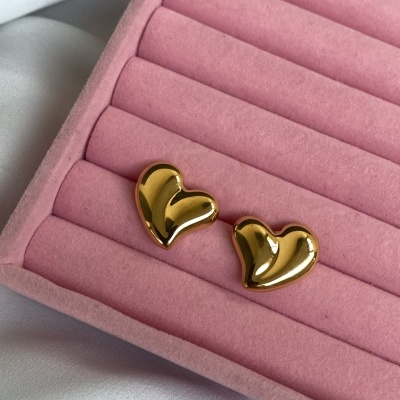 Brincos dourados em forma de coração sobre caixa rosa de veludo em tecido branco