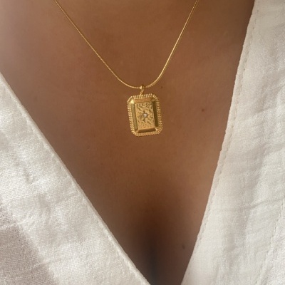 Colar dourado com pendente retangular usado com camisa branca