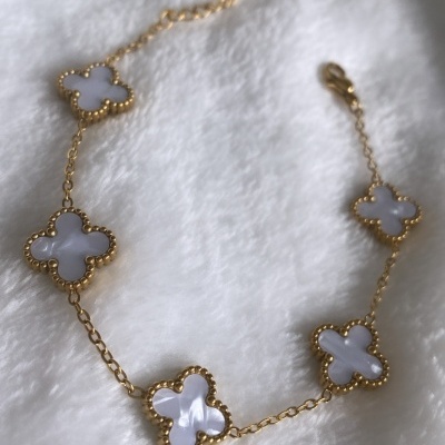 Pulseira dourada com pendentes em forma de trevo branco sobre tecido branco