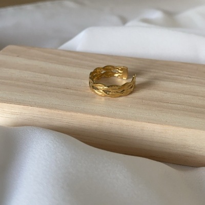 Anel dourado texturizado sobre base de madeira clara e fundo branco