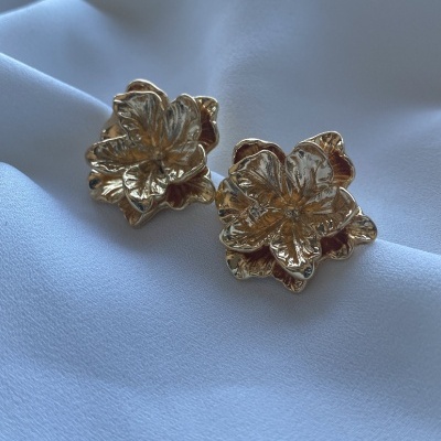 Brincos dourados em forma de flor sobre tecido branco