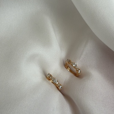 Brincos de argola dourados com pedras transparentes sobre tecido branco.