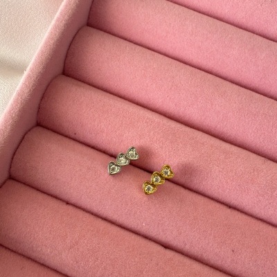 Brincos de corações em prata e dourado com pedras em suporte rosa de veludo.