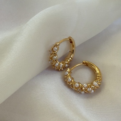 Brincos de argola dourados com pérolas e cristais sobre tecido branco