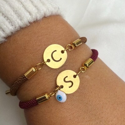 Pulseiras de corda com discos dourados e letras, uma com pendente olho turco, usadas no pulso