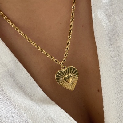 Colar dourado com pendente em forma de coração com relevo, sobre pele e camisa branca