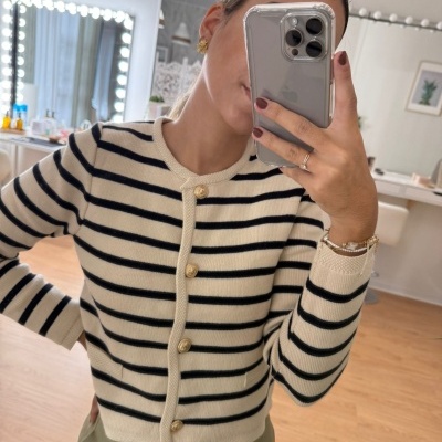 Cardigan creme com riscas pretas e botões dourados, calças verdes, ambiente interior com espelho iluminado