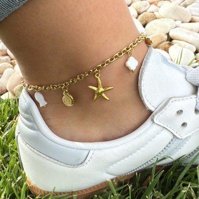 Tornozeleira dourada com pendentes de estrela do mar e conchas no tornozelo junto a sapato branco