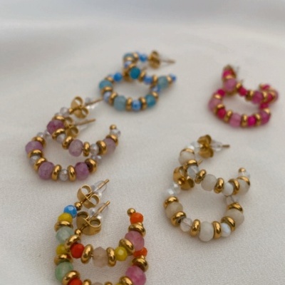 Seis pares de brincos coloridos em forma de argola sobre tecido branco.
