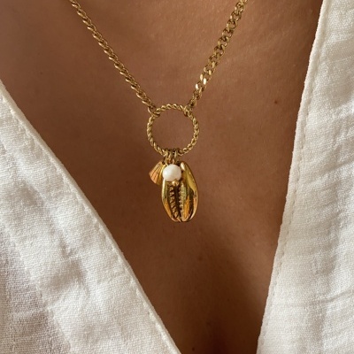 Colar dourado com pendente de conchas e pérola sobre camisa branca