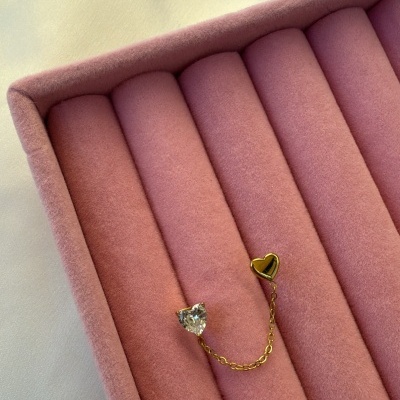 Brincos em forma de coração com corrente dourada numa caixa cor-de-rosa.