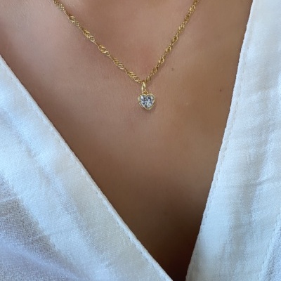 Colar dourado com pendente de coração de pedra transparente num pescoço com camisa branca