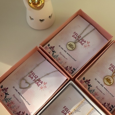 Colares em caixas cor-de-rosa com cartão Feliz Dia da Mãe e anjo decorativo branco com coração dourado.