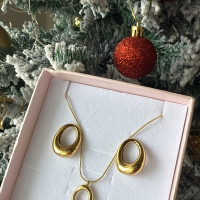 Conjunto de joalharia dourado com colar e brincos em forma oval numa caixa e árvore de Natal ao fundo