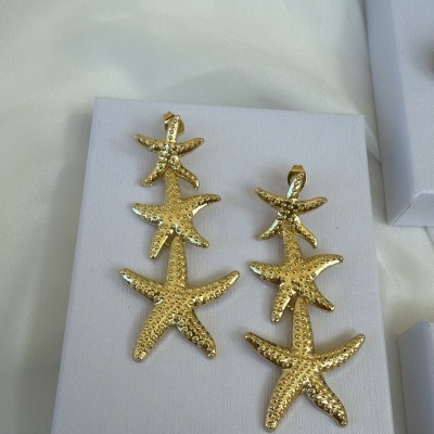 Brincos dourados em forma de estrelas do mar sobre caixa branca