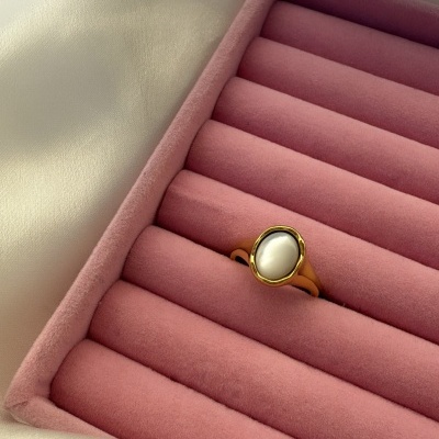 Anel dourado com pedra oval branca em caixa rosa acolchoada