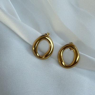 Brincos dourados ovais irregulares sobre tecido branco acetinado