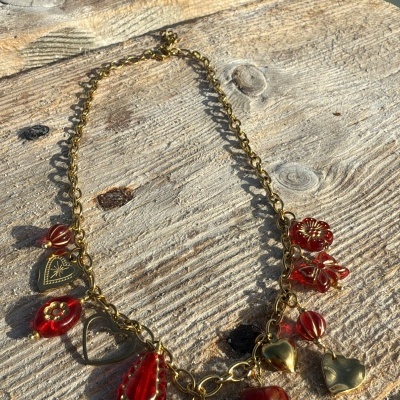 Colar dourado com pendentes vermelhos e dourados em madeira perto de água