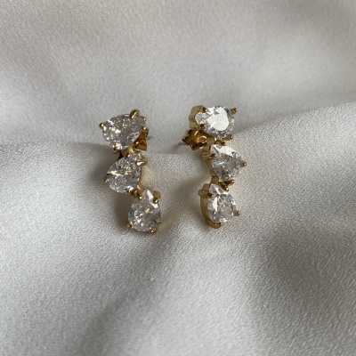 Brincos dourados com pedras transparentes sobre tecido branco