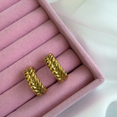 Brincos dourados ondulados numa caixa rosa sobre tecido branco