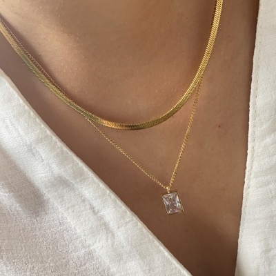 Colares dourados finos com pendente retangular translúcido sobre camisa branca