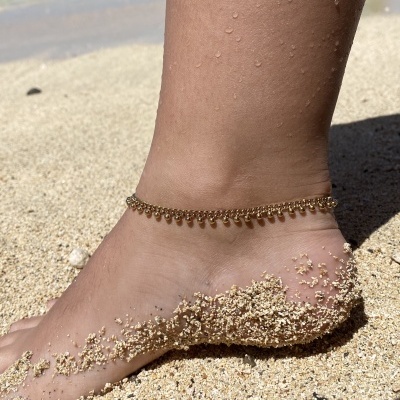 Tornozelo com pulseira dourada em areia de praia junto ao mar