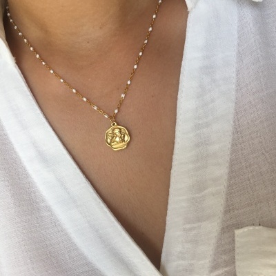 Colar dourado com pendente e pérolas em cima de camisa branca de linho
