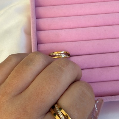 Anel dourado com pedras em dedo feminino e caixa rosa acolchoada