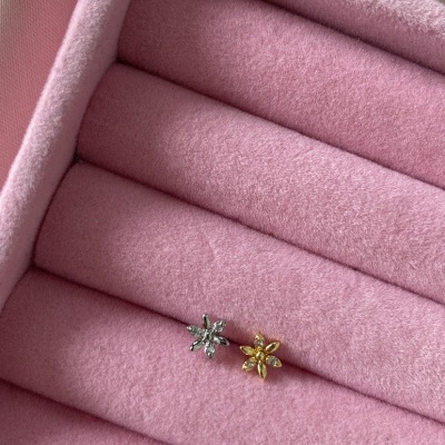 Brincos pequenos em forma de flor prateado e dourado numa caixa de veludo rosa