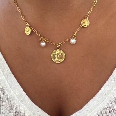 Colar dourado com medalhas e pérolas numa pessoa com uma t-shirt branca