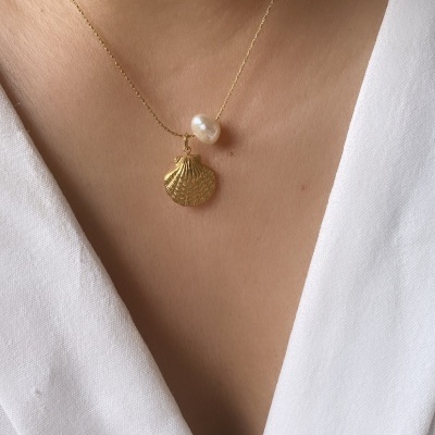 Colar com concha dourada e pérola em pescoço com vestido branco